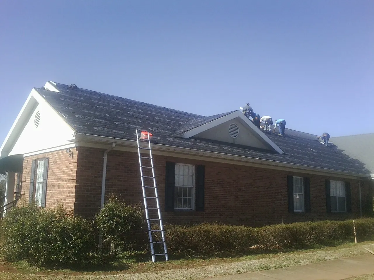 Crew tearing shingles off a brick ranch roof with a ladder set — Emergency Roof Repair work by our crew in Attleboro