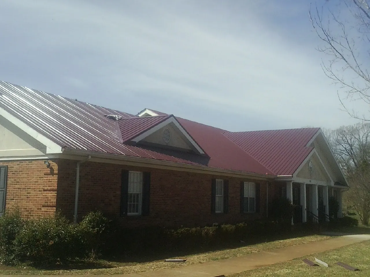 Red metal roof with gabled entries on a long brick building, from a Hail Damage Roof Repair job in Attleboro