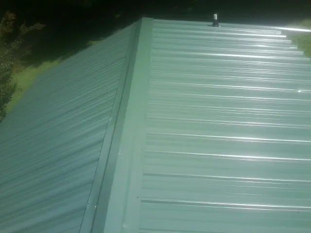 New green metal panels meeting at the ridge of a roof — Flat Roof Repair work by our crew in Attleboro