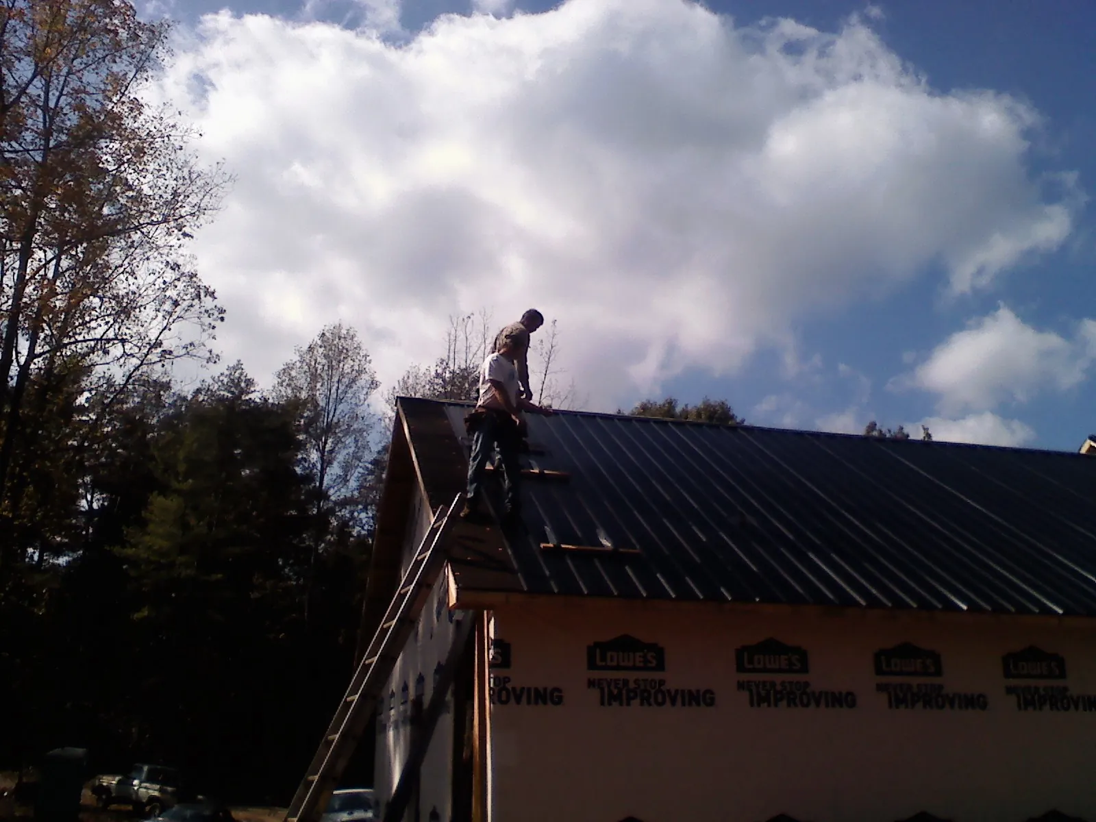 Roofer fastening dark metal panels high against a cloudy sky, from a Roof Inspection job in Attleboro