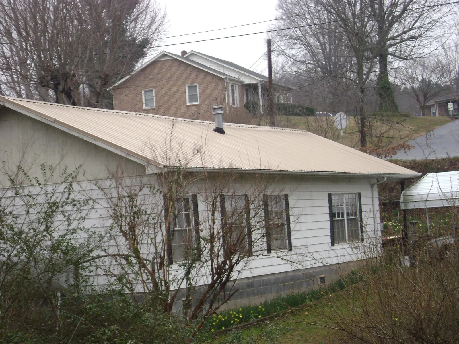 Tan metal roof on a white sided house set into a hillside — Commercial Roofing by Roofing Brothers in Attleboro